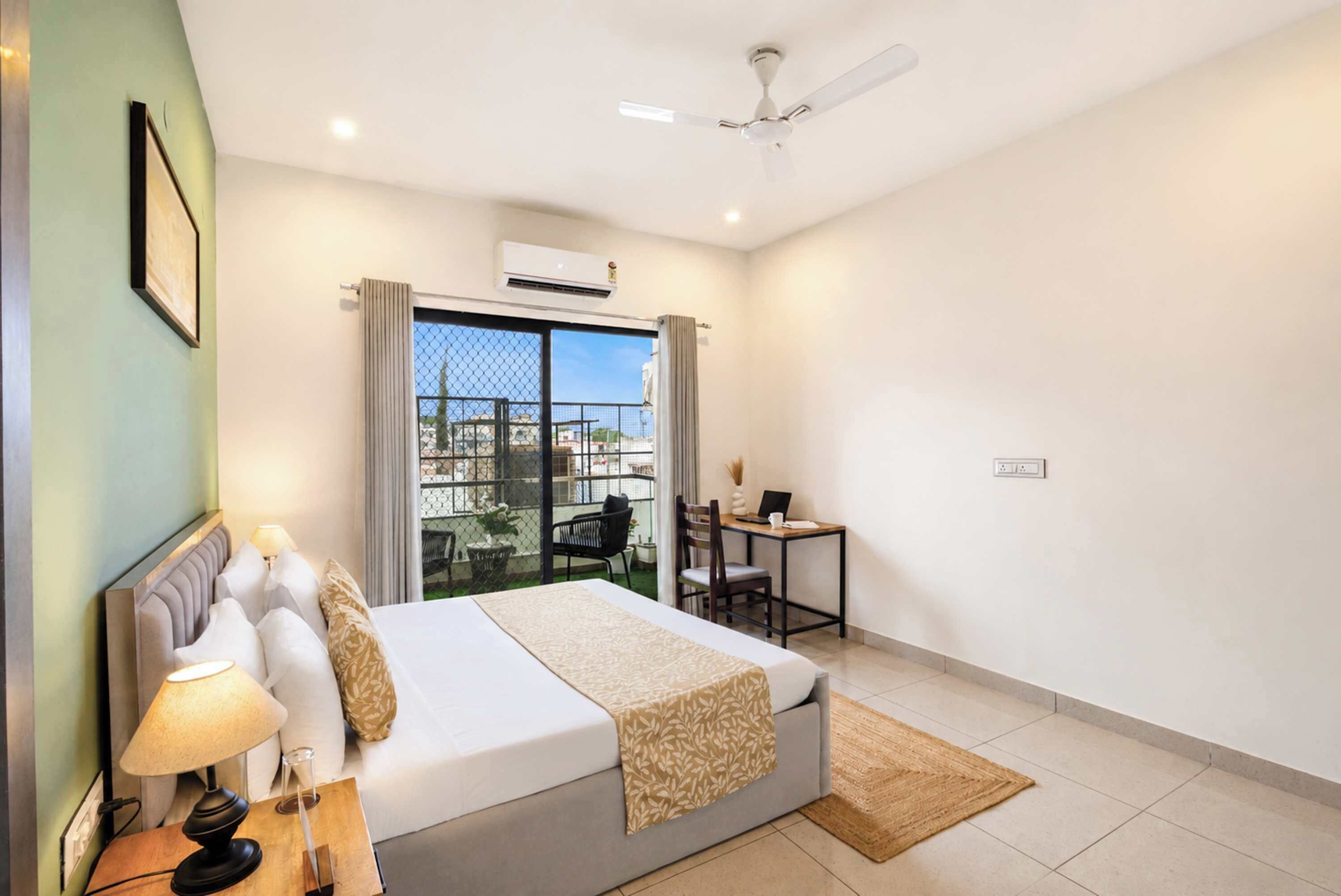 Habitación de hotel con cama, escritorio, silla, ventilador de techo y vistas por la ventana.