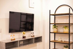 A modern living room with a flat-screen TV mounted on the wall, a marble countertop, and a black metal shelving unit with decorative items and plants.
