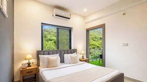 A modern bedroom with a large bed, a window with a view of greenery, and an air conditioning unit on the wall.