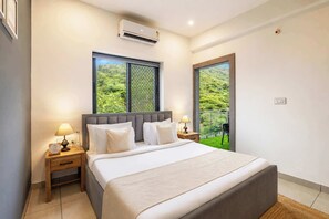 A modern bedroom with a large bed, a window with a view of greenery, and an air conditioning unit on the wall.