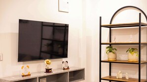 A modern living room with a flat-screen TV mounted on the wall, a marble countertop, and a black metal shelving unit with decorative items and plants.
