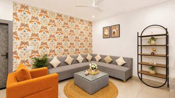 A modern living room with a grey sofa, orange armchair, and a coffee table with a vase of flowers.
