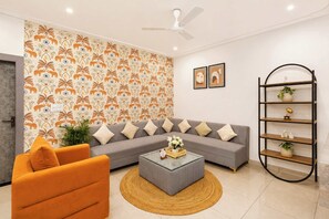 Un salon moderne avec un canapé gris, un fauteuil orange et une table basse agrémentée d’un vase de fleurs.