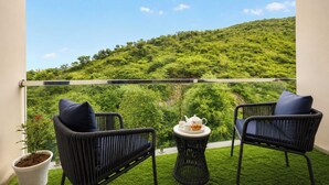 A balcony with two wicker chairs, a small round table with a teapot, cups, and a pastry, and a potted plant.
