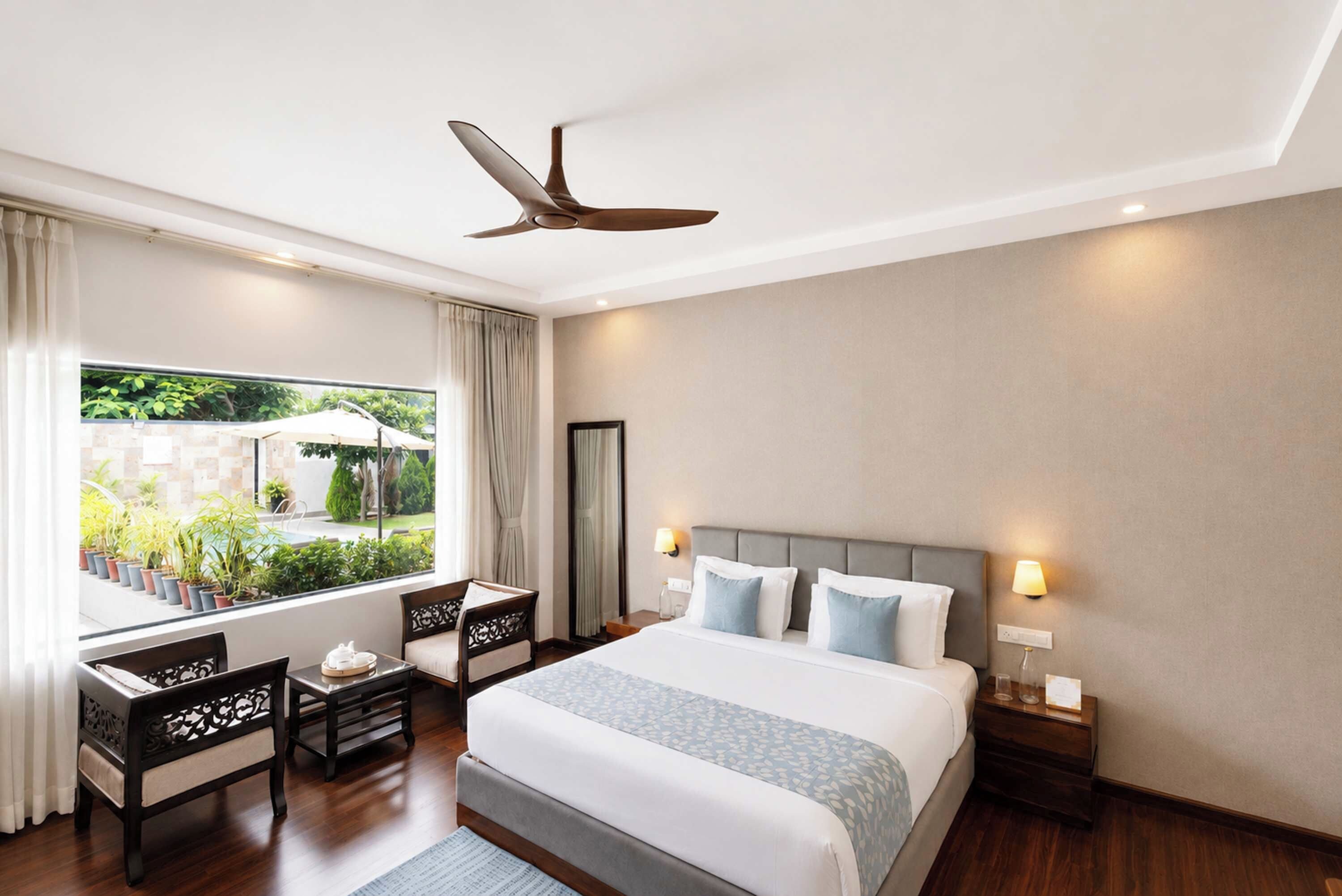 Habitación de hotel con cama, mesitas de noche, escritorio, silla, ventilador de techo y ventana con vistas a zonas verdes.