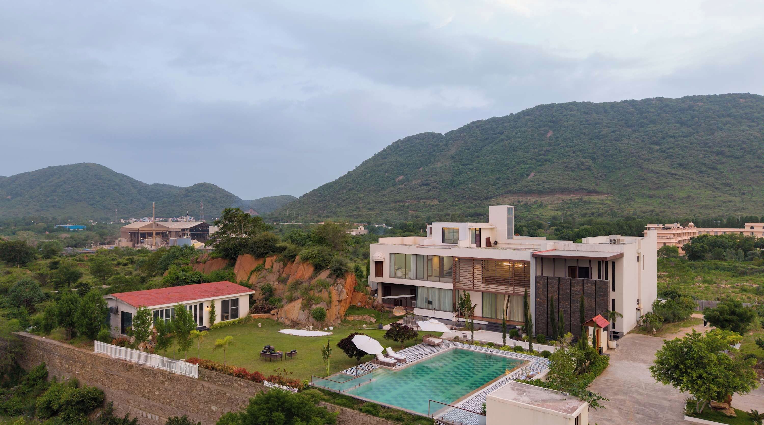 A modern two-story building with a swimming pool, surrounded by greenery and hills.