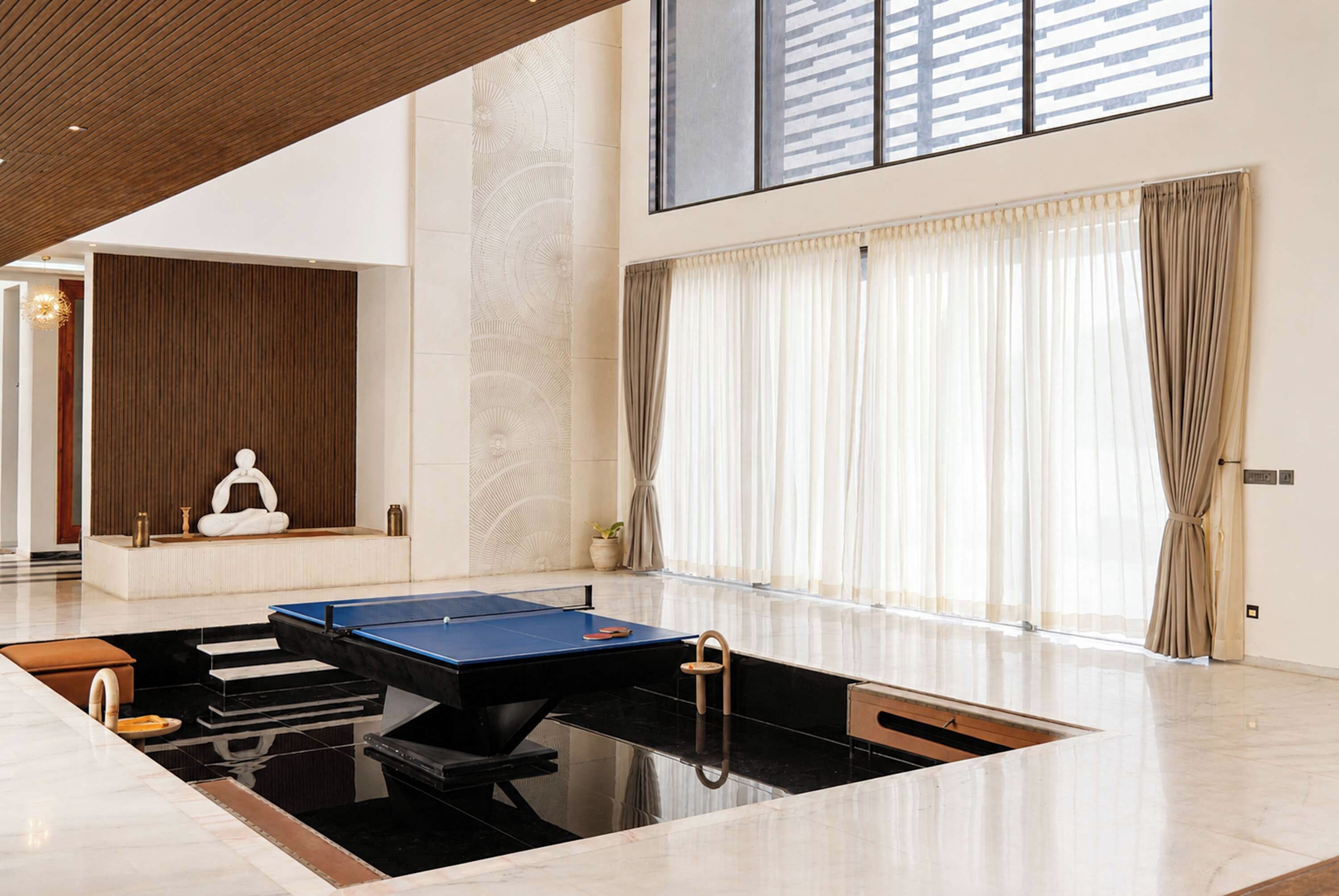 A spacious room with a ping pong table, a meditation area, and large windows with curtains.