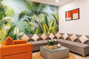 A living room with a large sofa, orange armchair, and a glass coffee table with a plant.