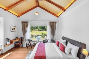 A bedroom with a bed, bedside table, lamp, window with curtains, and a view of greenery outside.