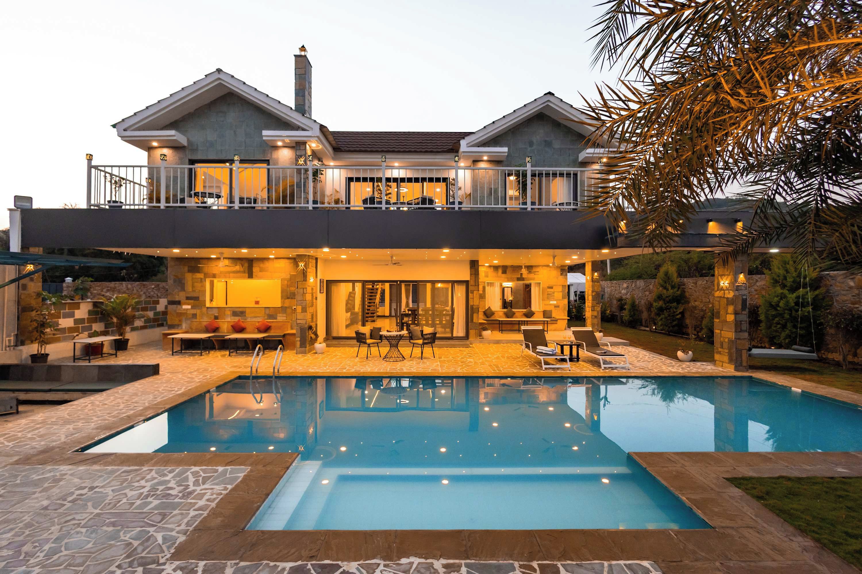 A two-story house with a swimming pool, outdoor seating, and a well-lit interior.