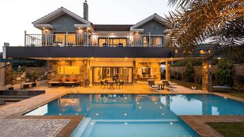 A two-story house with a swimming pool, outdoor seating, and a well-lit interior.