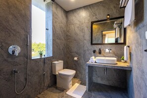 A modern bathroom with a marble wall, a toilet, a shower, a sink, and a large mirror.