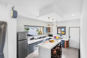 A modern kitchen with a central island, stainless steel appliances, pendant lighting, and a view through the window.
