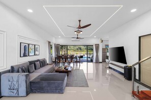 A modern living room with a sectional sofa, a dining area, a flat-screen TV, and a ceiling fan.