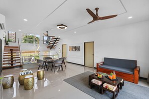 Un vaste espace de vie comprenant un canapé, une table basse et une table à manger avec des chaises. On y trouve également un escalier avec une rampe et un ventilateur de plafond.