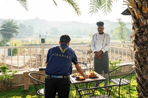 A chef and a server at a table with food and drinks, overlooking a scenic landscape.