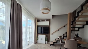 Ein modernes Wohnzimmer mit Treppe, Essbereich und Wand-Fernseher.