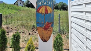 Ein Holzschild mit Strandmotiv und dem Schriftzug 'Life is Better at the Beach', befestigt an einem weißen Pfosten.