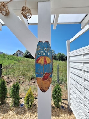 Ein Holzschild mit Strandmotiv und dem Schriftzug 'Life is Better at the Beach', befestigt an einem weißen Pfosten.