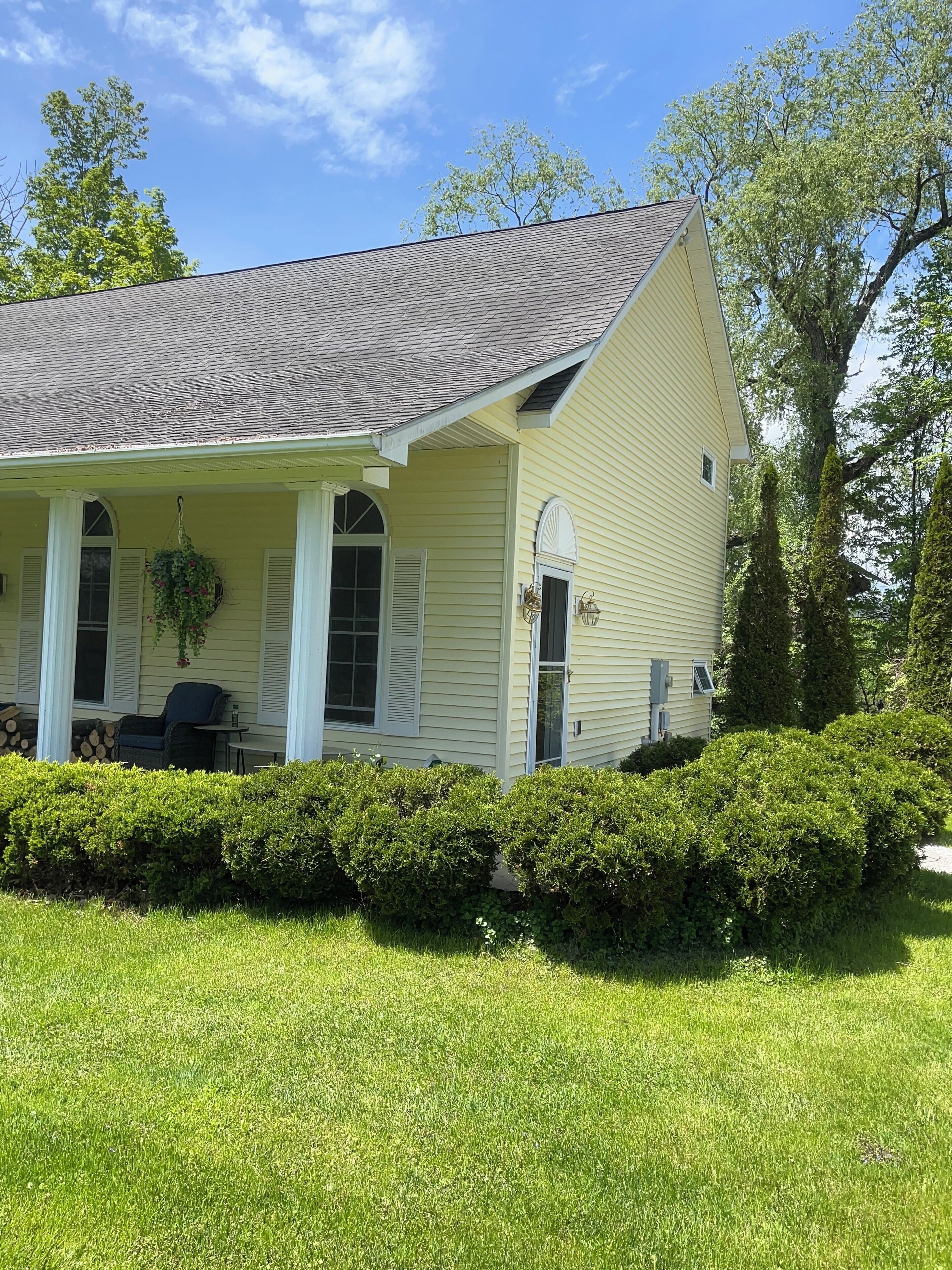 A single-story house with a gabled roof, a covered porch with a chair, and a well-maintained lawn.