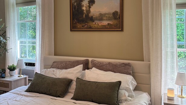 Un dormitorio con una cama grande, un cuadro en la pared y una ventana con cortinas.