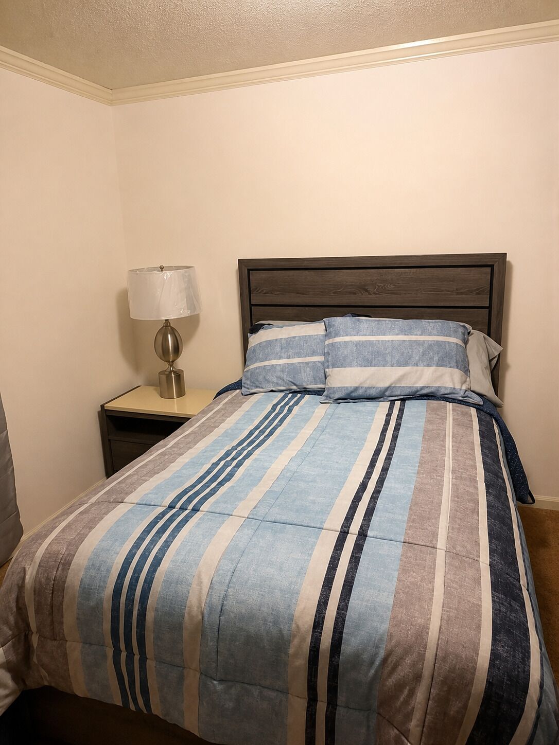 A bed with a striped bedspread, a wooden headboard, and a bedside table with a lamp.