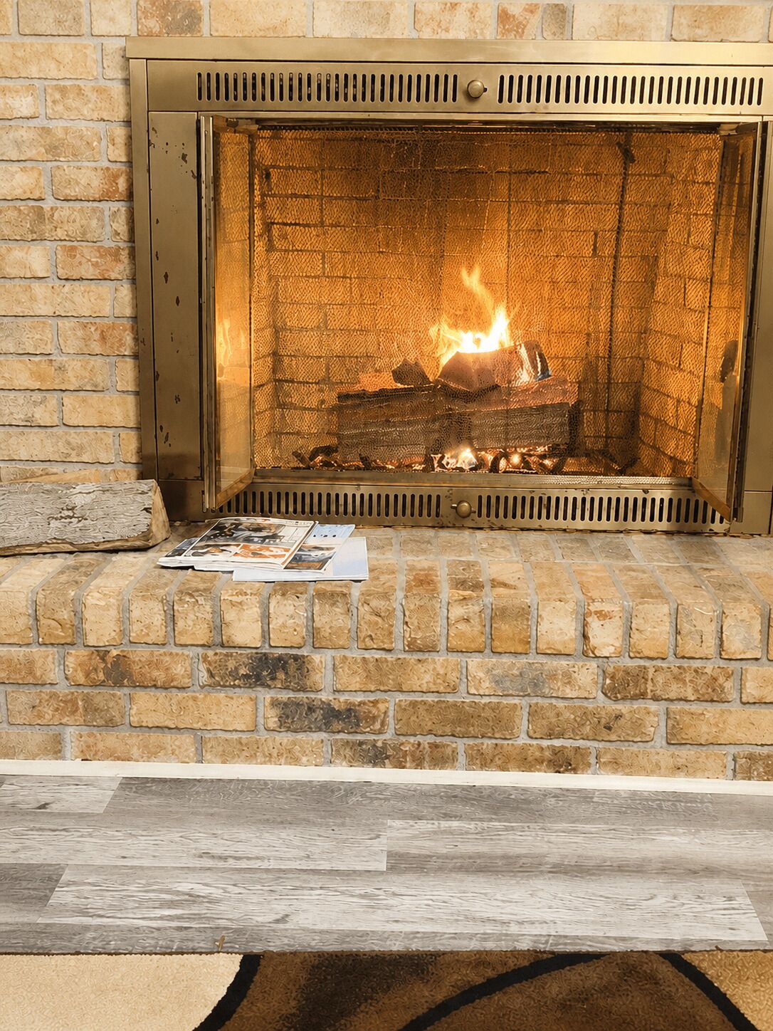 A fireplace with a brick surround, a magazine on the mantel, and a wooden log fire.