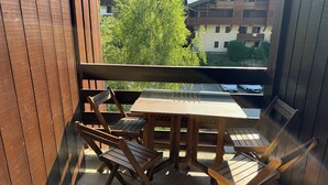 Ein Balkon mit Holzmöbeln, darunter ein Tisch und Stühle, mit Blick auf eine Wohngegend mit Häusern und parkenden Autos.