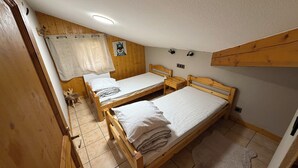 Ein kleiner, gemütlicher Raum mit zwei Holzbetten, einer Holztür, einem kleinen Tisch und einer Wandleuchte.