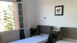 A room with two single beds, a window with a view of trees, a radiator, and a framed picture on the wall. - A house in the heart of the vineyards and at the foot of Mont Ventoux (Mormoiron)