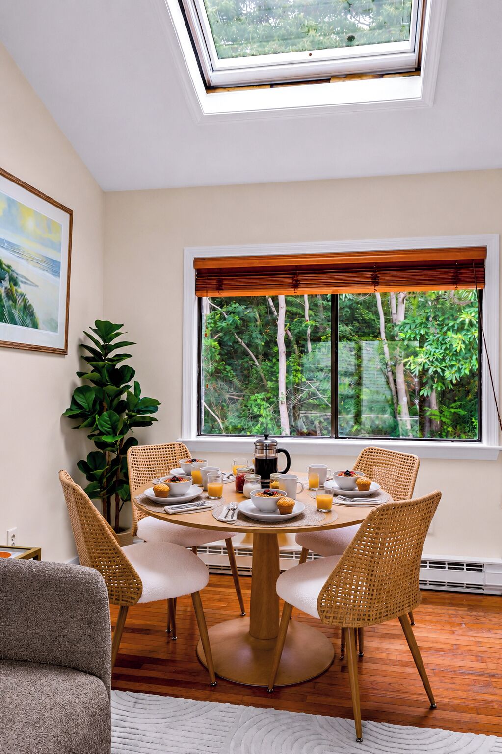 Un coin repas avec une table ronde, des chaises en osier, une machine à café et une vue sur la verdure par une fenêtre.