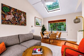Ein Wohnzimmer mit einer Couch, einem Esstisch mit Stühlen, einem Deckenventilator, einem Oberlicht und einem Bild an der Wand.
