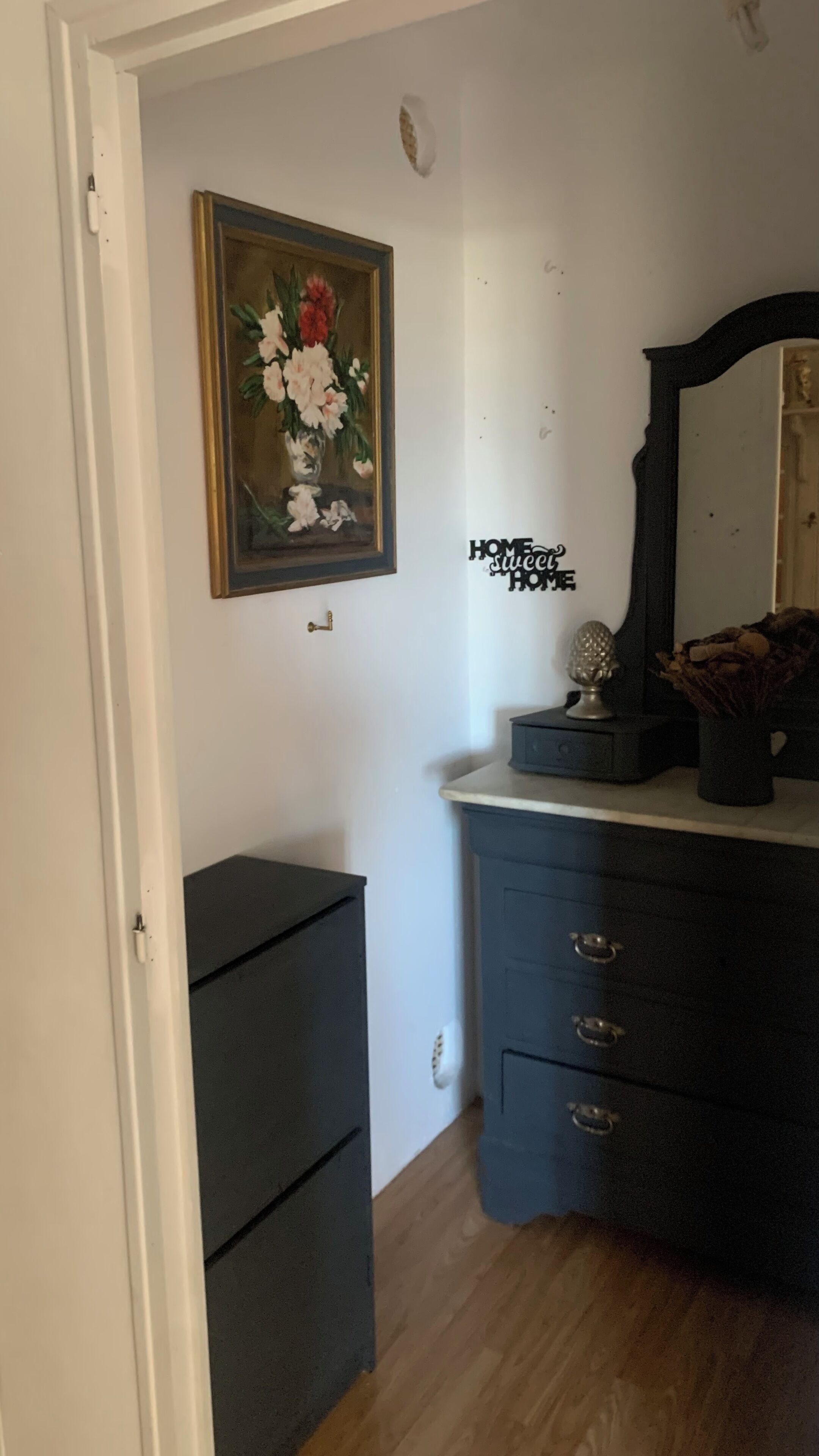 A room with a dark dresser, a mirror, a framed painting, and a small decorative item on the dresser.
