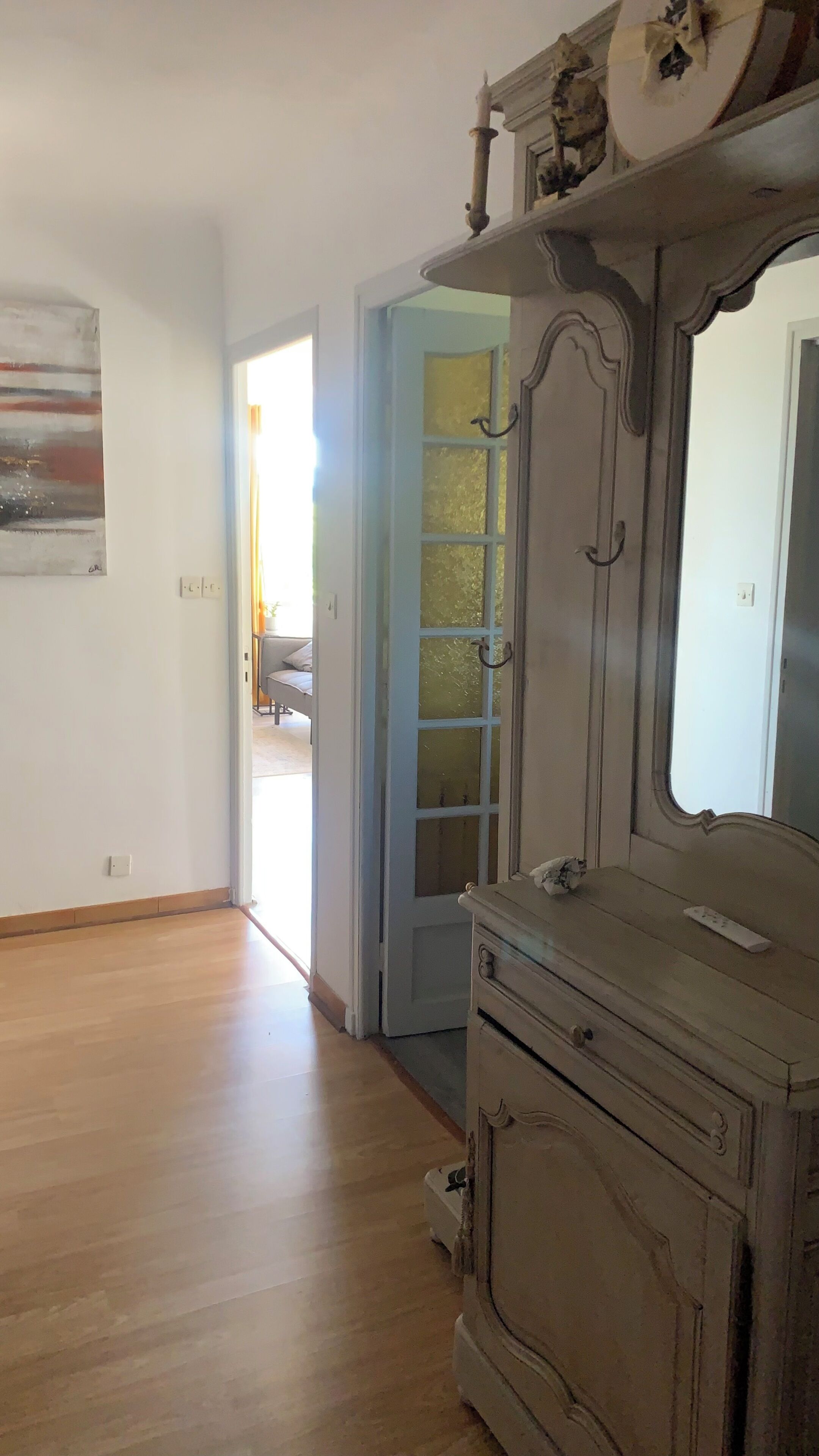 Una habitación con piso de madera, un aparador con espejo y una puerta que da a otra estancia.