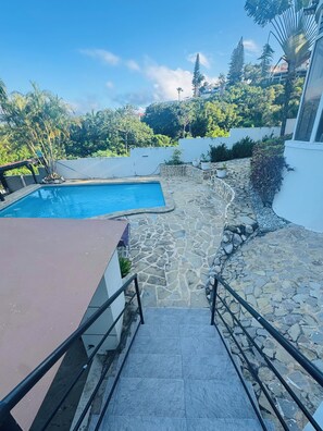 A stone pathway leading to a swimming pool with a view of lush greenery and a building in the background. - Villa La Dueña, Cofresi Beach, Puerto Plata (Puerto Plata)