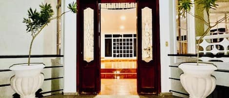 A hallway with a dark wooden door, two white urns with plants, and a tiled floor.