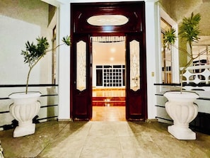 A hallway with a dark wooden door, two white urns with plants, and a tiled floor. - Villa La Dueña, Cofresi Beach, Puerto Plata (Puerto Plata)