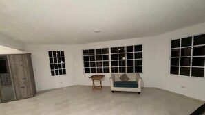 Ein geräumiges Zimmer mit Fliesenboden, einer Couch, einem kleinen Holztisch und mehreren Fenstern.