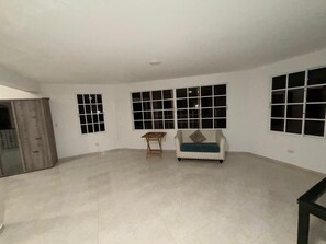A spacious room with a tiled floor, a sofa, a small wooden table, and multiple windows. - Villa La Dueña, Cofresi Beach, Puerto Plata (Puerto Plata)