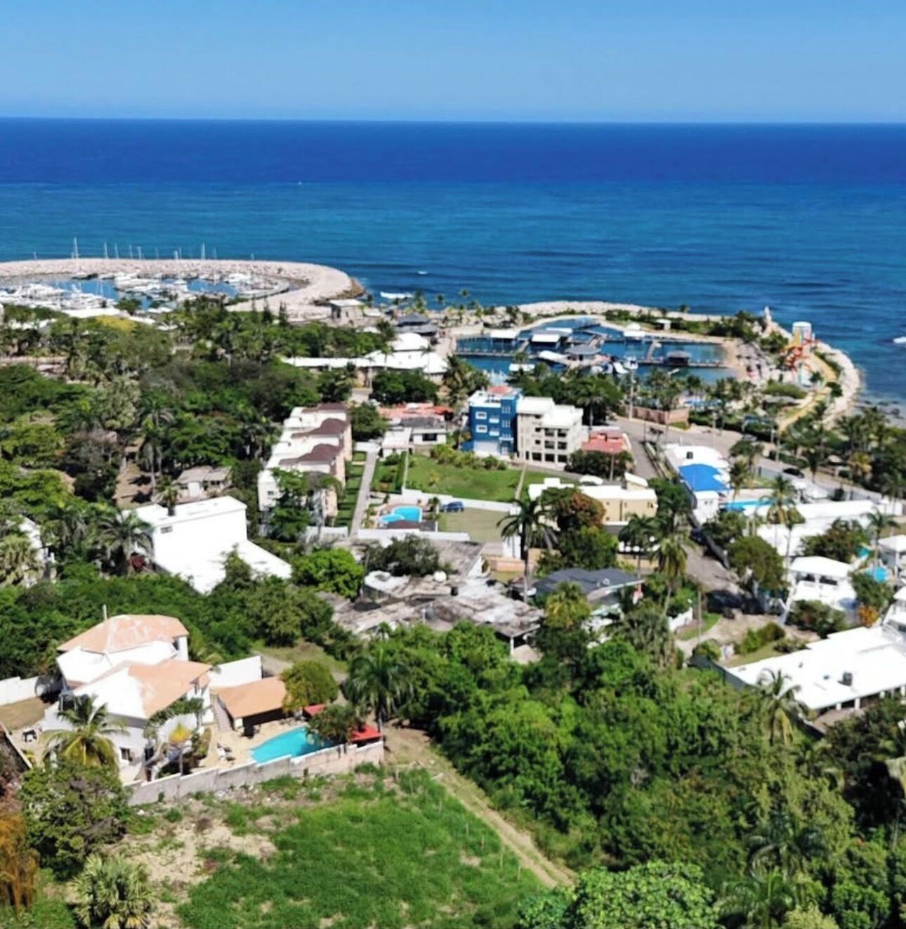 An aerial view of a coastal resort with multiple buildings, a beach, and a pool area.