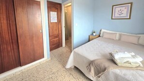 A bedroom with a bed, a nightstand, a wooden wardrobe, and a door leading to another room.