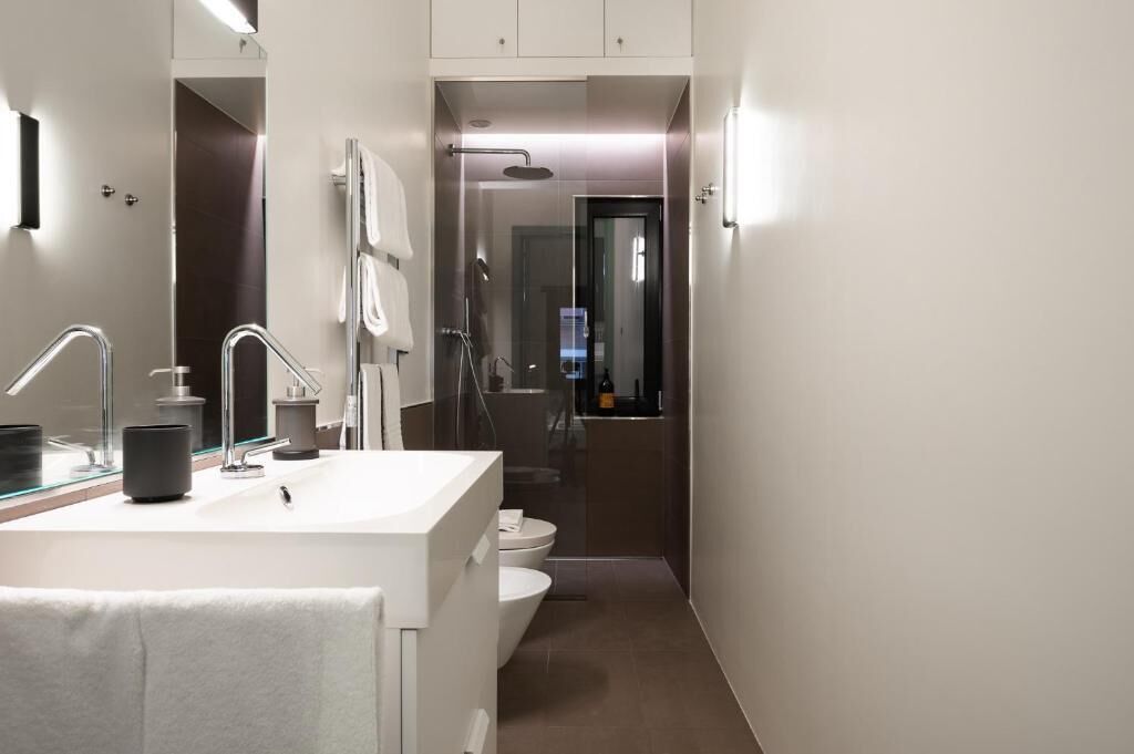 A modern bathroom with a large mirror, a white sink, a shower, and a toilet.