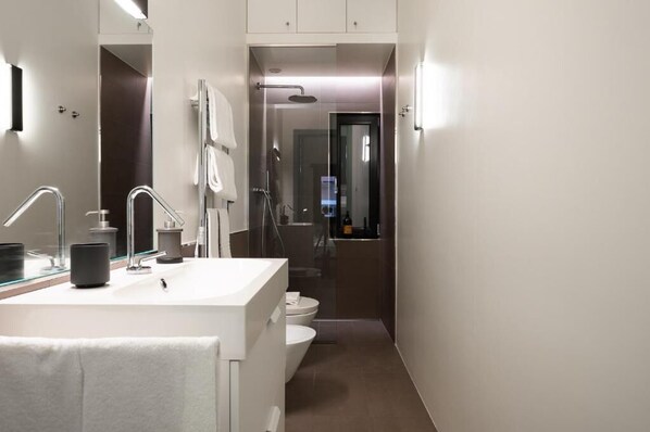 A modern bathroom with a large mirror, a white sink, a shower, and a toilet.