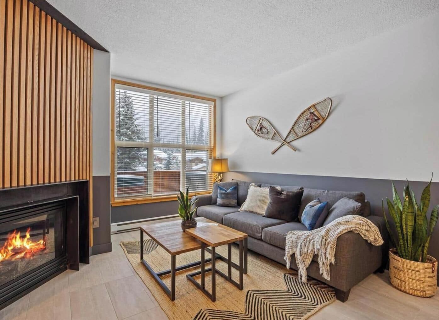 A modern living room with a fireplace, a sofa, a coffee table, and a large window with blinds.