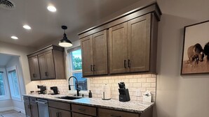 A modern kitchen with wooden cabinets, a marble countertop, and a stainless steel trash can.