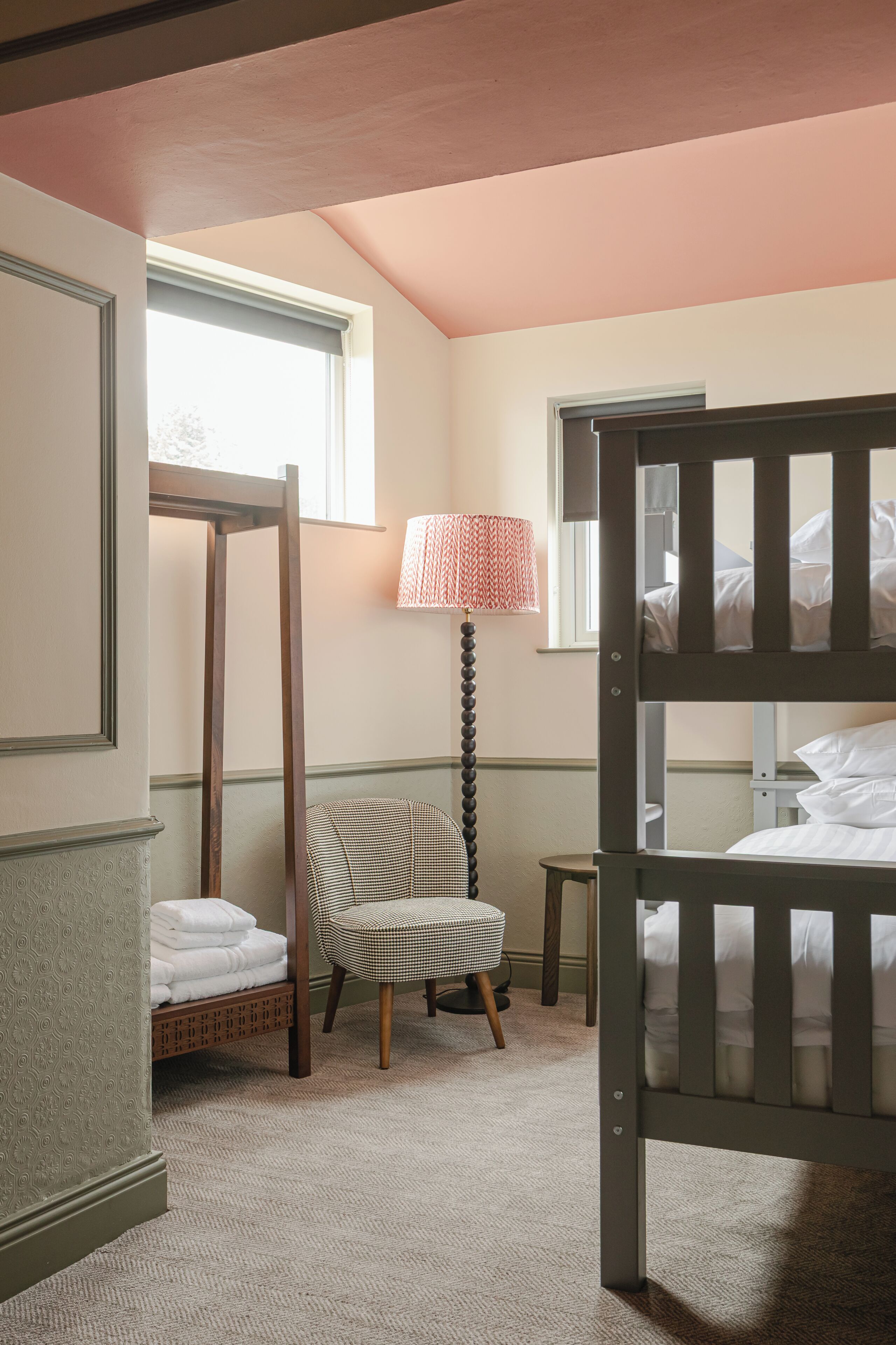 A bedroom with bunk beds, a chair, a lamp, and a window.