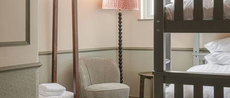 A bedroom with bunk beds, a chair, a lamp, and a window.