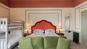 A hotel room with a bunk bed, a large bed with green upholstered headboard, two bedside tables with lamps, a large mirror, and a radiator. - Avoca House (Newcastle)
