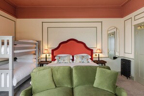 Hotelkamer met een stapelbed, een groot bed met een groen gestoffeerde hoofdeinde, twee nachtkastjes met lampen, een grote spiegel en een radiator.