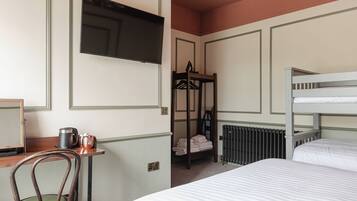 A hotel room with a bunk bed, a desk with a chair, a radiator, and a television mounted on the wall.